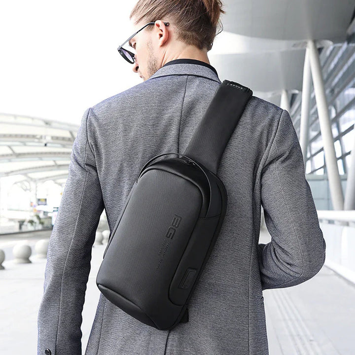 Man wearing sunglasses and gray blazer with black crossbody sling backpack in urban modern setting