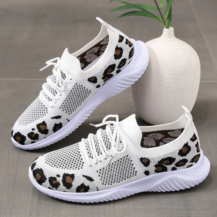 White knit sneakers with leopard print accents and white flexible soles on gray surface