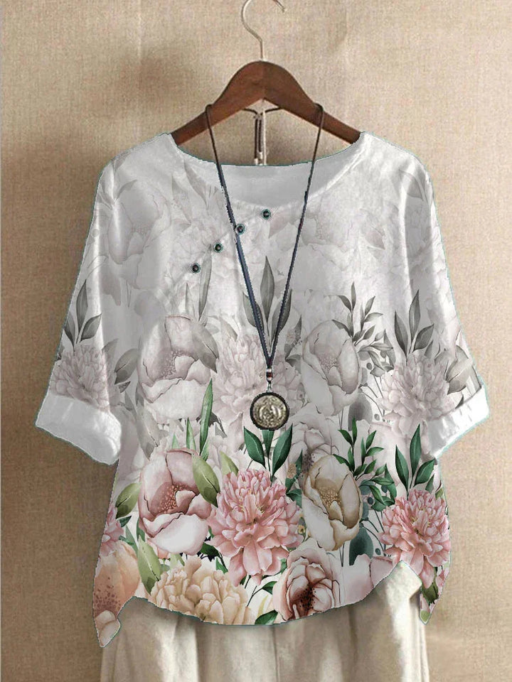 White floral blouse with pink and beige peonies on wooden hanger, paired with pendant necklace