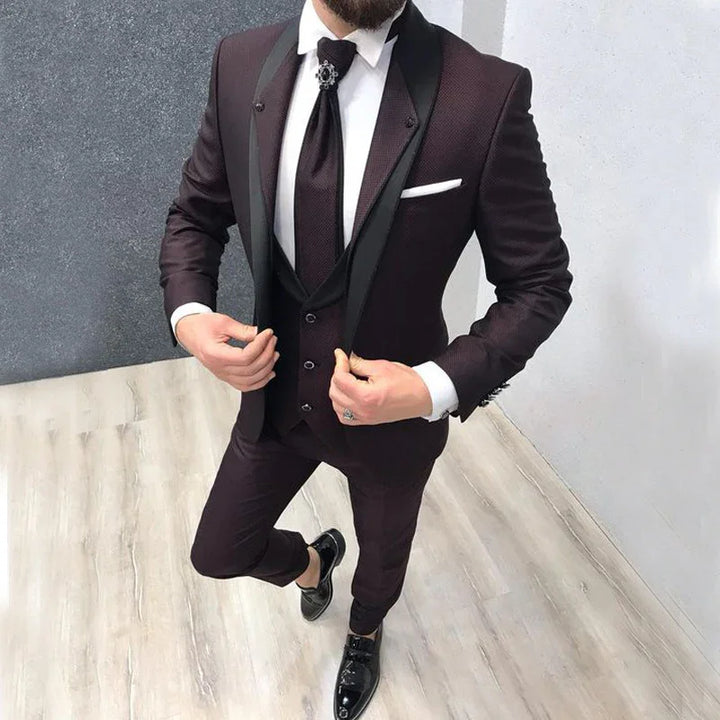 Man wearing a tailored dark burgundy three-piece suit with black satin lapels, black tie, white dress shirt, and black dress shoes.