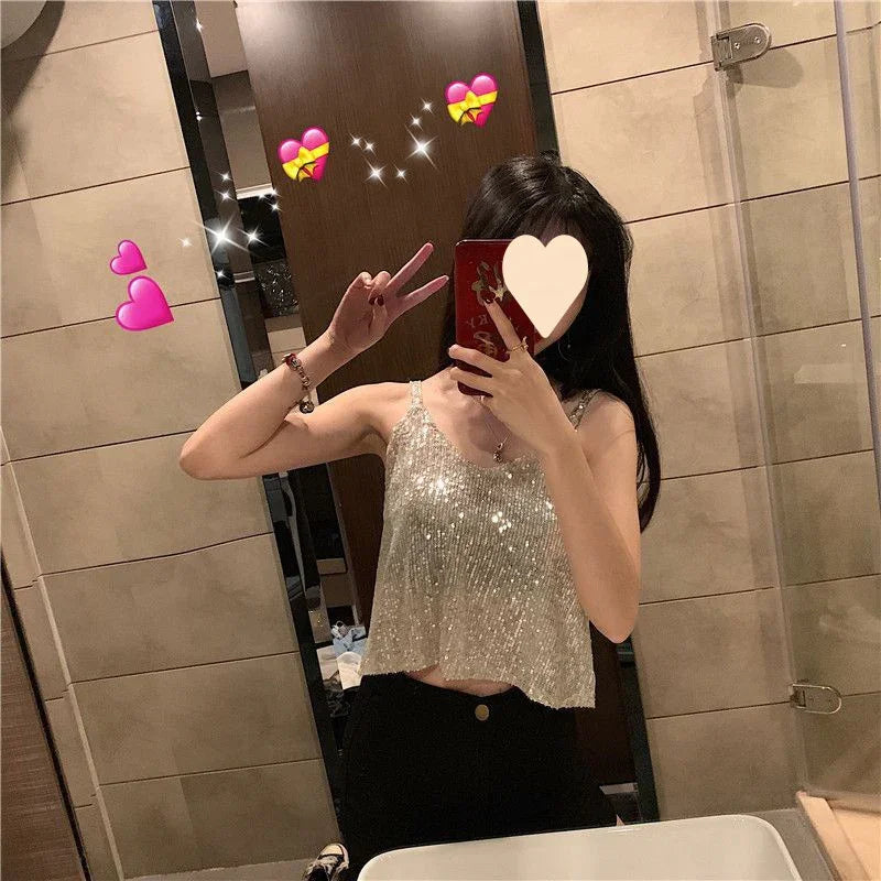 Woman taking mirror selfie in bathroom wearing silver sequin tank top and black pants with heart emojis