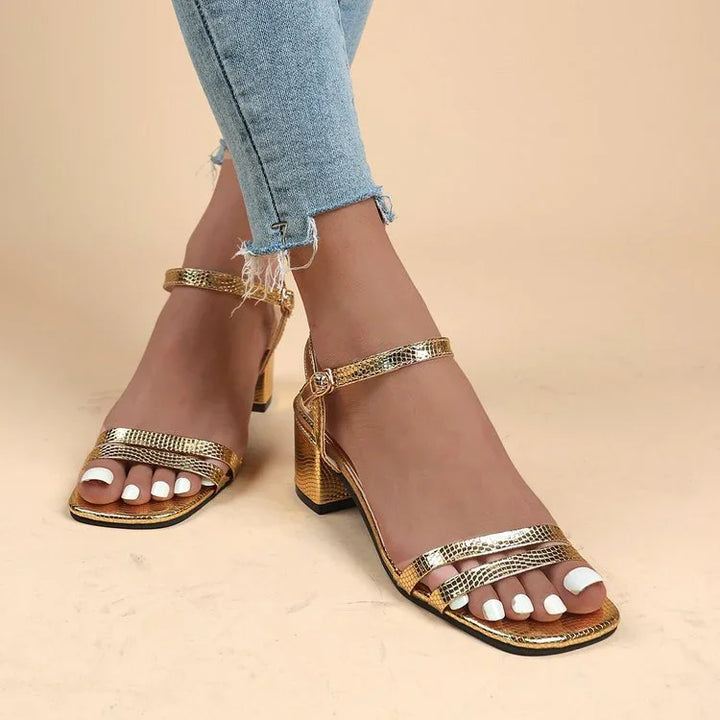 Woman wearing gold metallic block heel sandals with ankle straps and white nail polish, paired with frayed hem jeans