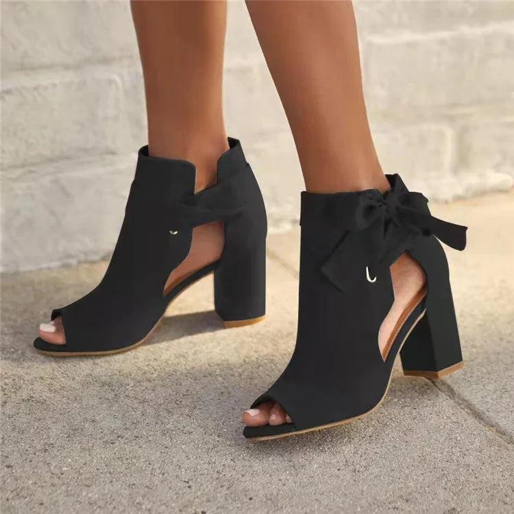 Black open-toe high heel ankle boots with cutouts and bow ties on sidewalk