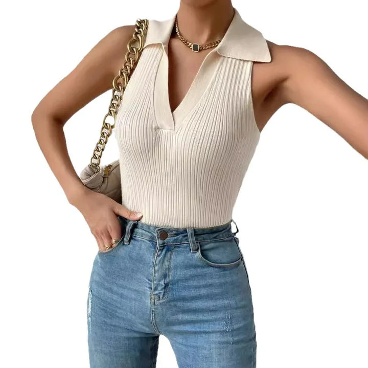 Woman wearing a sleeveless cream ribbed knit top with collar, blue high-waisted jeans, gold chain necklace, and beige handbag