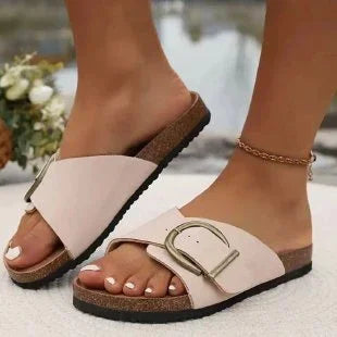 Close-up of feet wearing stylish beige cross-strap sandals with large buckle on cork sole