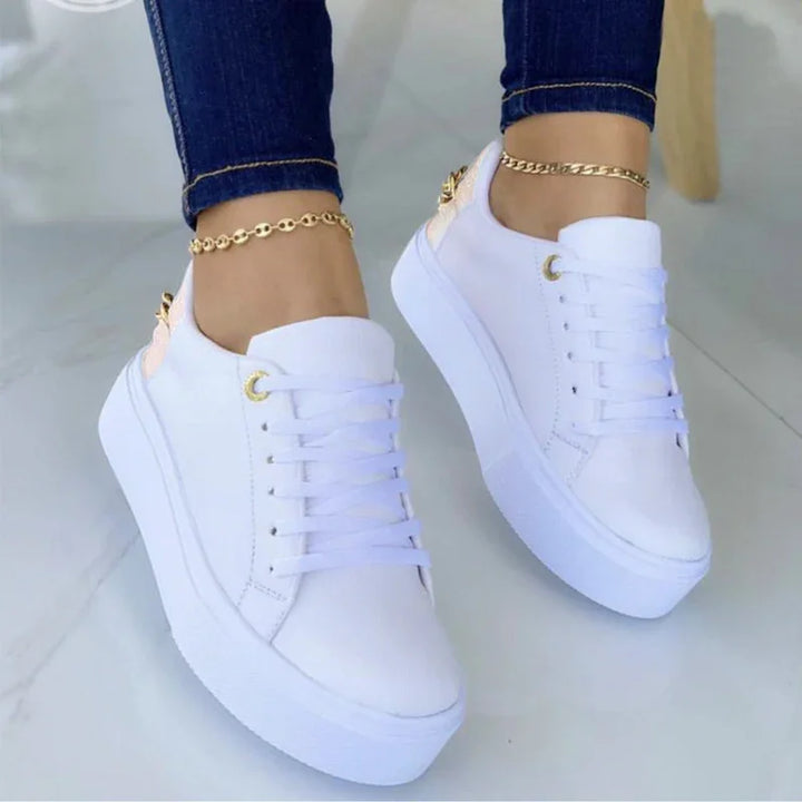 White platform sneakers worn with dark skinny jeans and gold anklets on a light floor