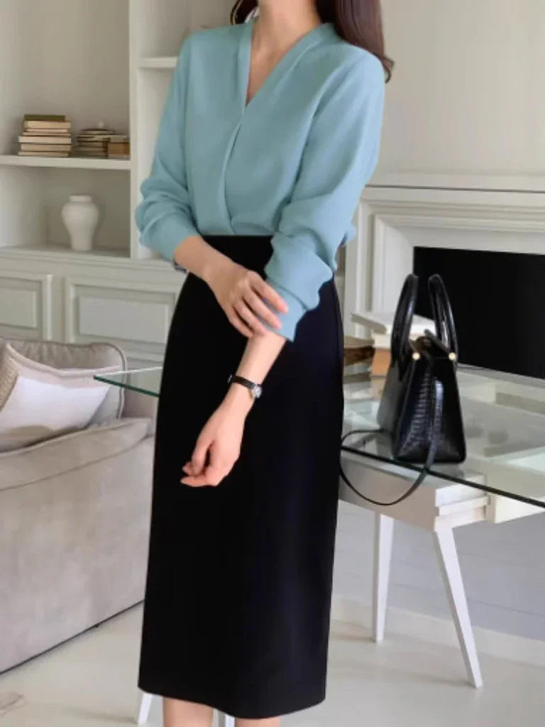 Woman wearing light blue blouse and black midi skirt indoors with glass table and black handbag