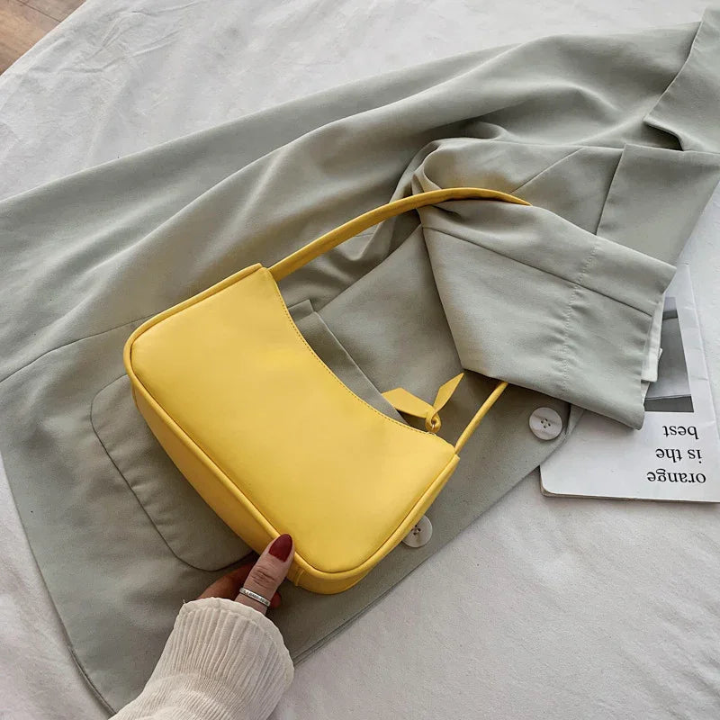 Yellow leather handbag on light gray blazer with hand holding bag on white surface