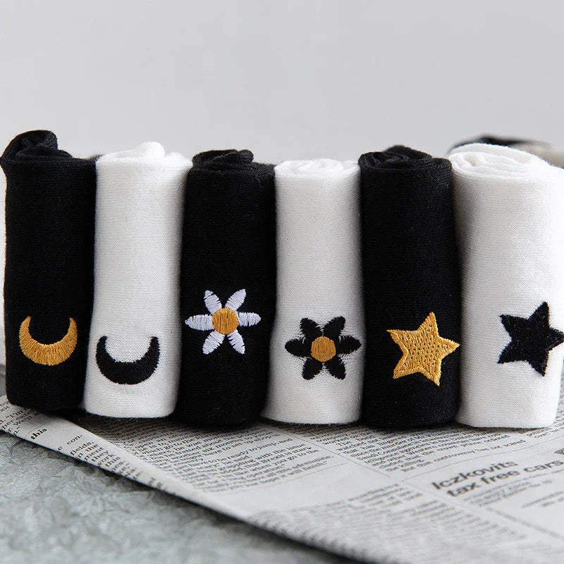 Rolled black and white socks with embroidered moon, flowers, and star designs on newspaper