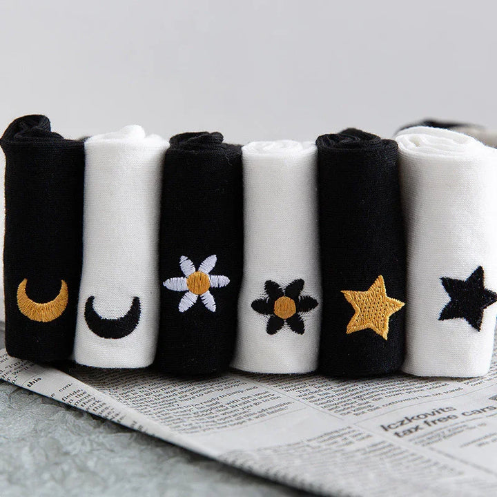 Rolled black and white socks with embroidered moon, flowers, and star designs on newspaper
