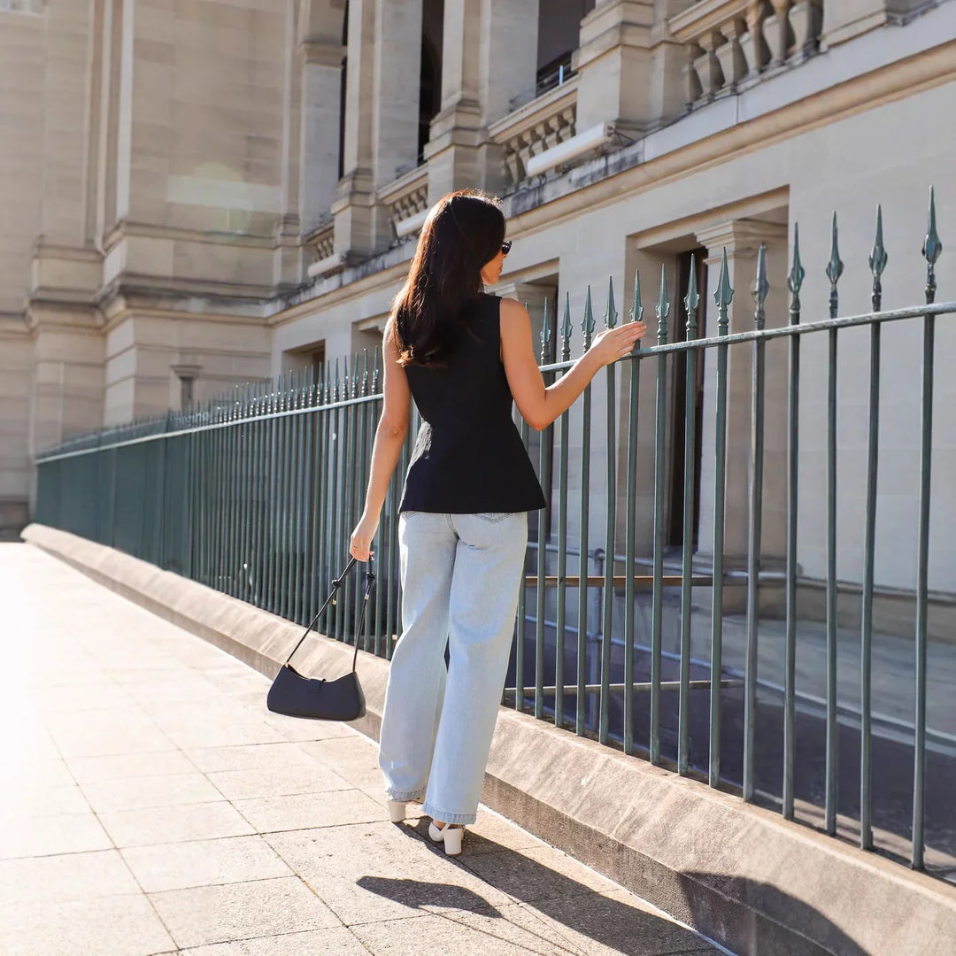 Woman in black sleeveless top and light blue jeans walking by wrought iron fence near stone building