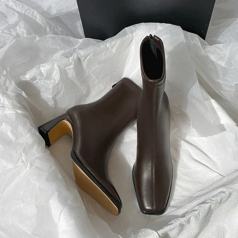 pair of dark brown leather ankle boots with square toes and block heels on white fabric