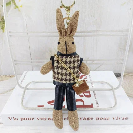 Knitted rabbit keychain with houndstooth sweater and leather pants, holding miniature brown purse
