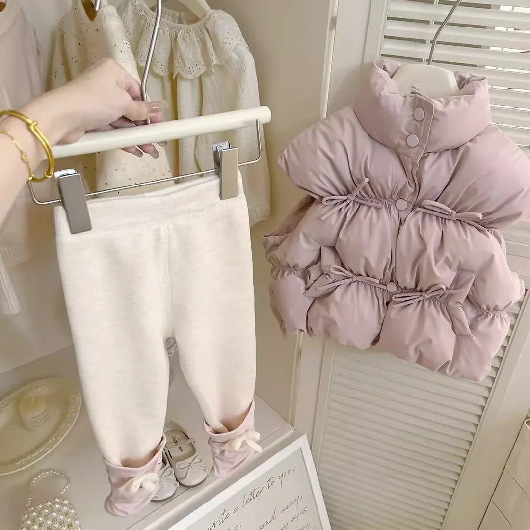 Hand holding white baby leggings with pink booties next to pink puffer baby jacket on hanger