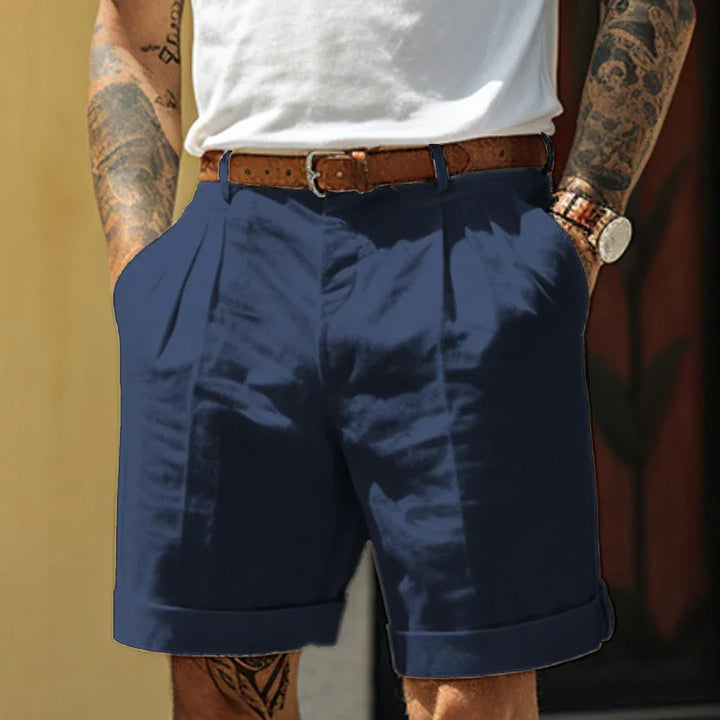 Man wearing navy blue cuffed shorts with a brown leather belt and white t-shirt, visible arm tattoos