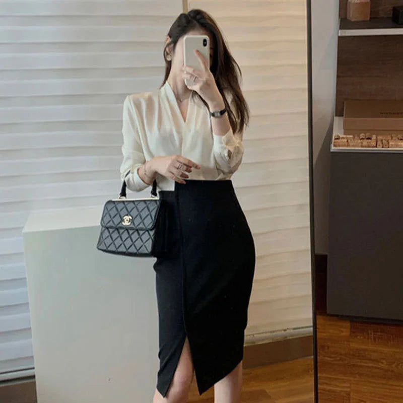 Woman in white blouse and black slit pencil skirt holding black quilted handbag taking mirror selfie