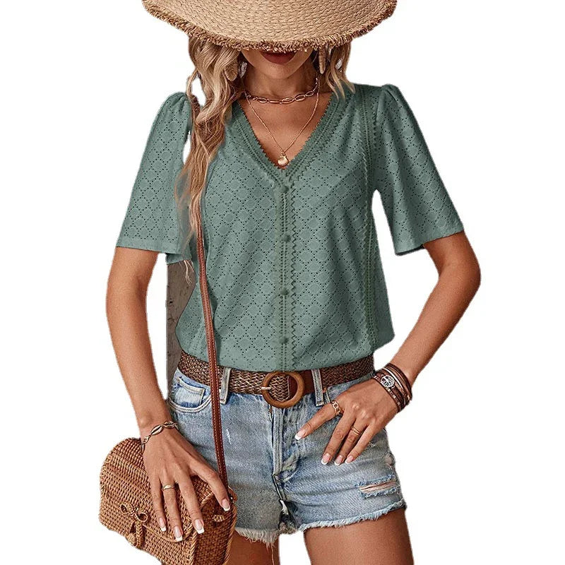 Woman wearing sage green eyelet blouse with V-neck, denim shorts, straw hat, and woven bag