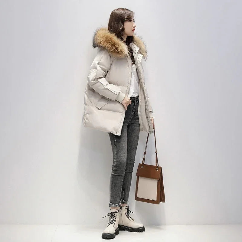 Woman wearing beige puffer jacket with fur hood, gray skinny jeans, cream boots, holding brown tote bag