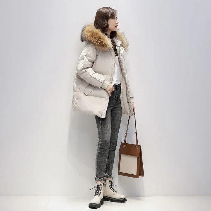 Woman wearing beige puffer jacket with fur hood, gray skinny jeans, cream boots, holding brown tote bag