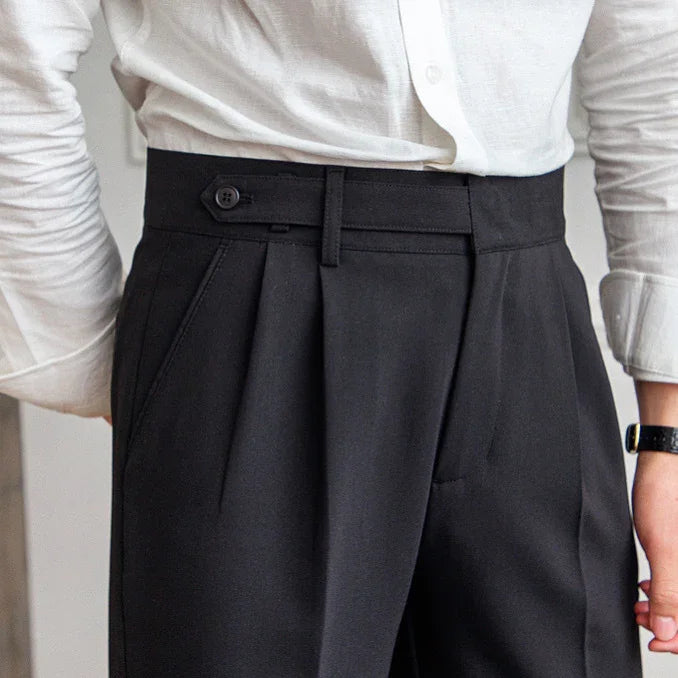 close-up of black high-waisted trousers with side adjuster button and pleats, worn with white shirt