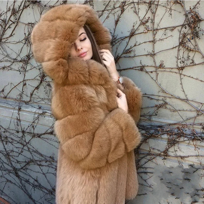 Woman wearing a luxurious brown fur coat with a large hood, posing against a wall covered with dry vine branches