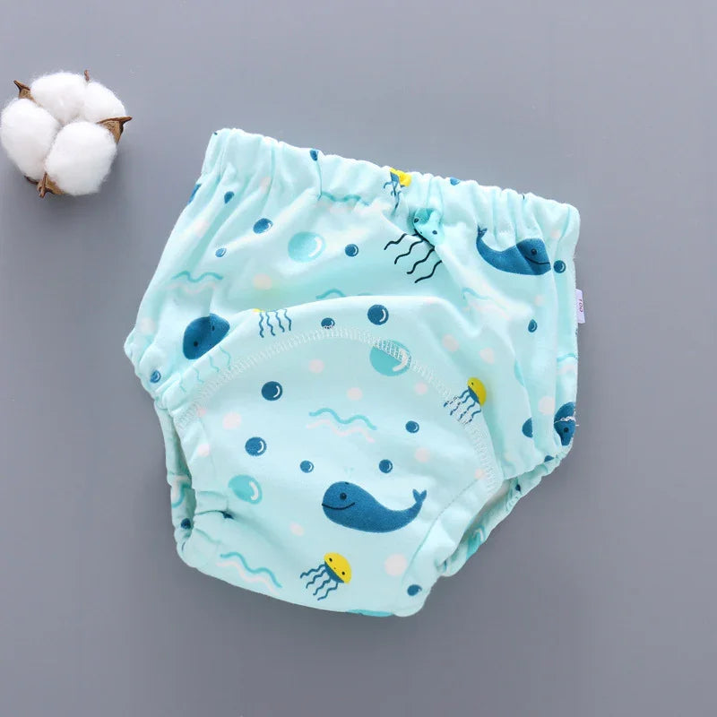 Light blue reusable baby diaper with whale and jellyfish print on gray background beside cotton boll