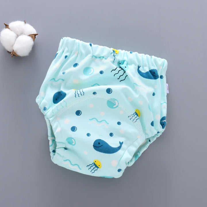 Light blue reusable baby diaper with whale and jellyfish print on gray background beside cotton boll