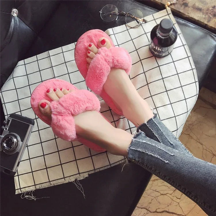 Person wearing pink fuzzy slippers with red nail polish, sitting on black leather sofa with sunglasses and camera nearby