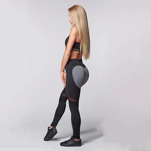 Woman in black and grey heart-shaped leggings and black sports bra with long blonde hair in studio