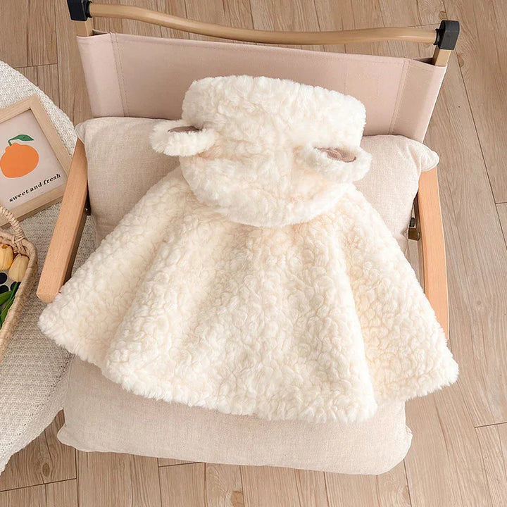 Cream-colored fluffy toddler cape with hood and bear ears on wooden chair with cushion