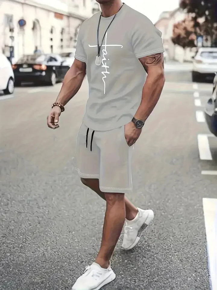 Man in gray 'Faith' t-shirt and matching shorts walking on city street wearing white sneakers and accessories