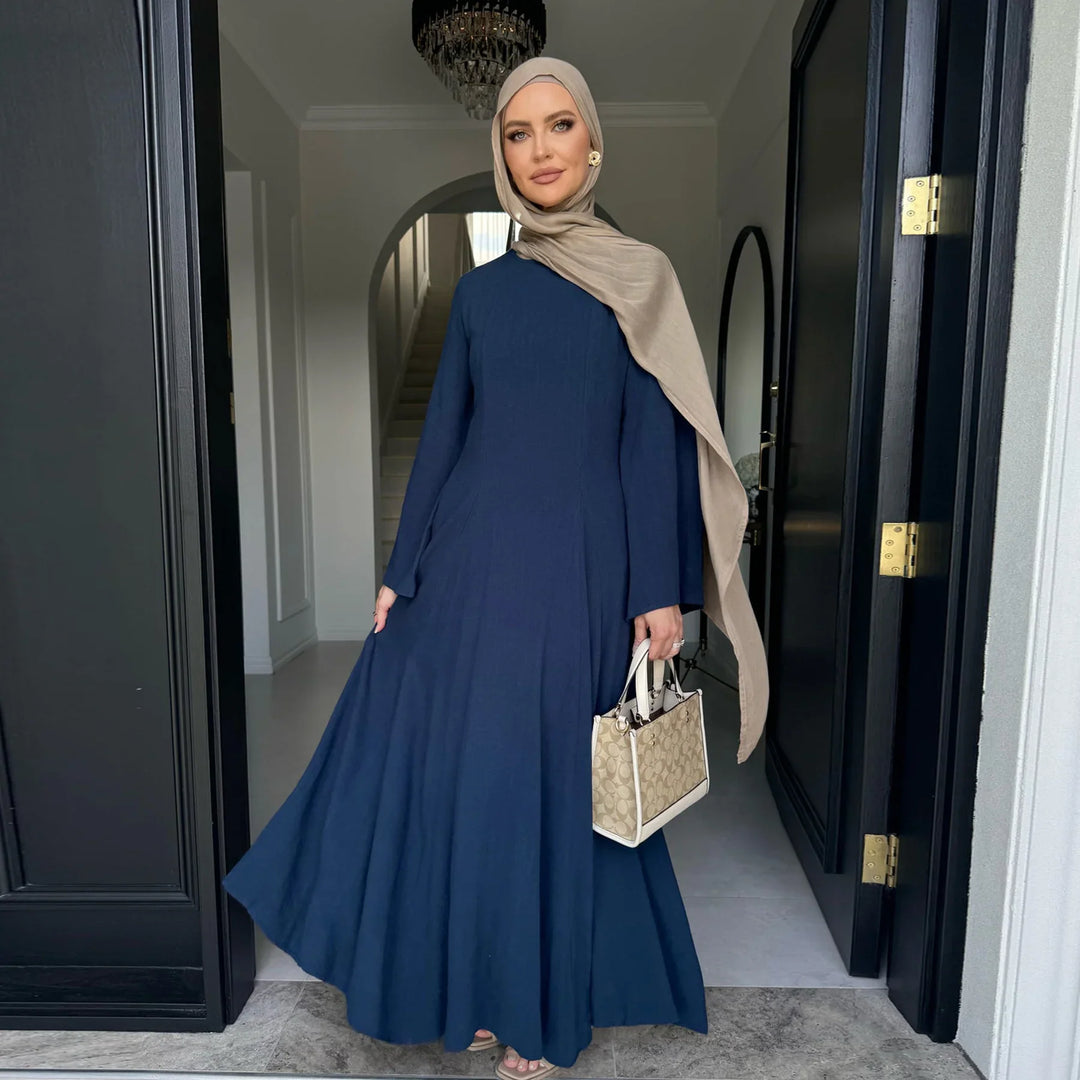 Woman in a navy blue abaya and beige hijab holding a beige handbag at a doorway