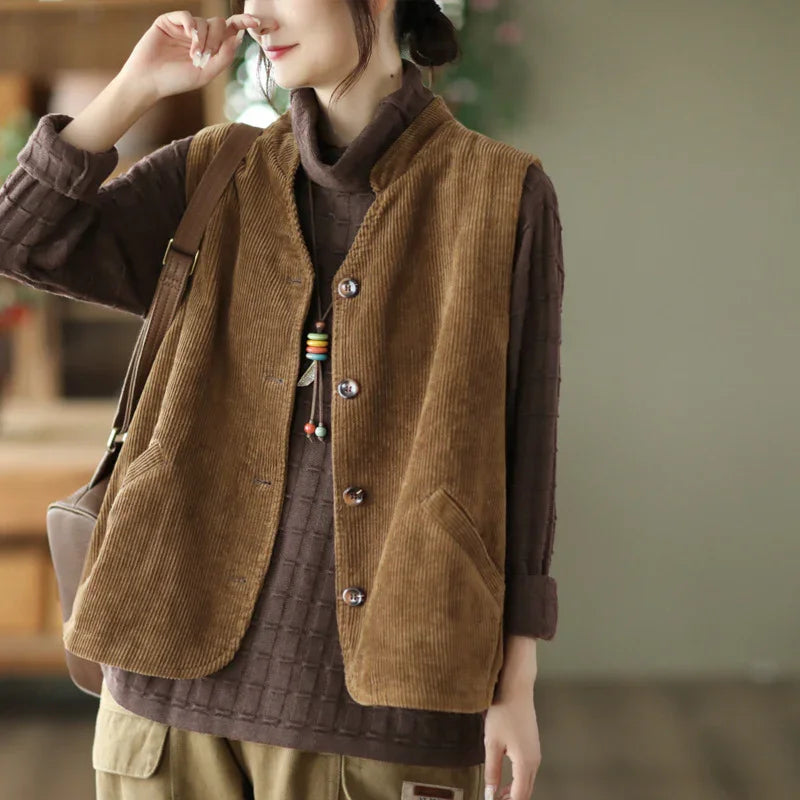Woman wearing a brown corduroy buttoned vest over a dark brown textured sweater with beige pants and a shoulder bag
