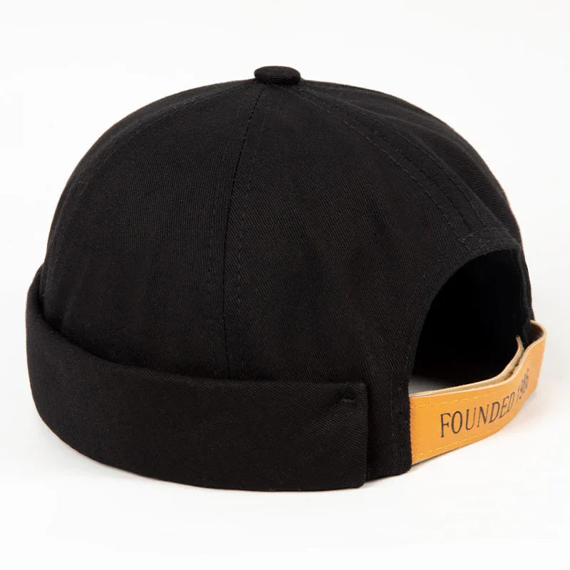 Black beanie-style cap with folded brim and tan leather adjustable strap reading 'FOUNDED'