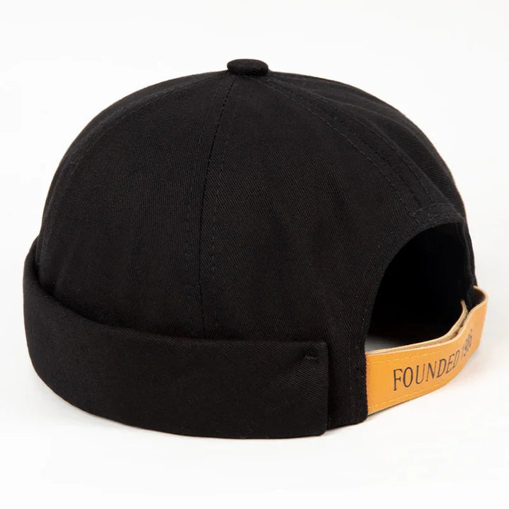 Black beanie-style cap with folded brim and tan leather adjustable strap reading 'FOUNDED'