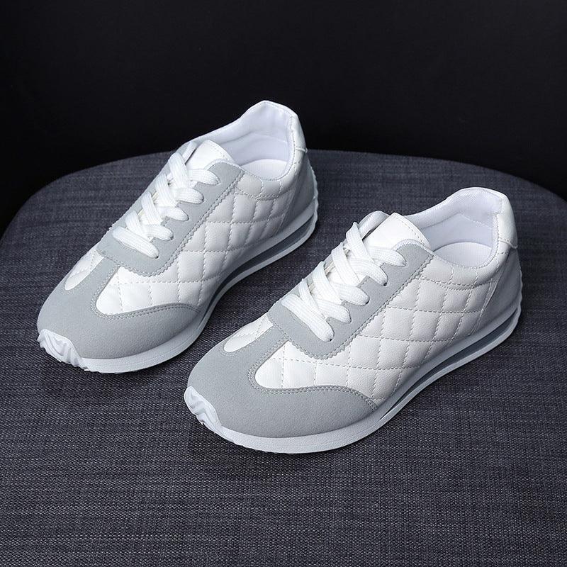 Pair of white and grey quilted sneakers with white laces on dark fabric surface