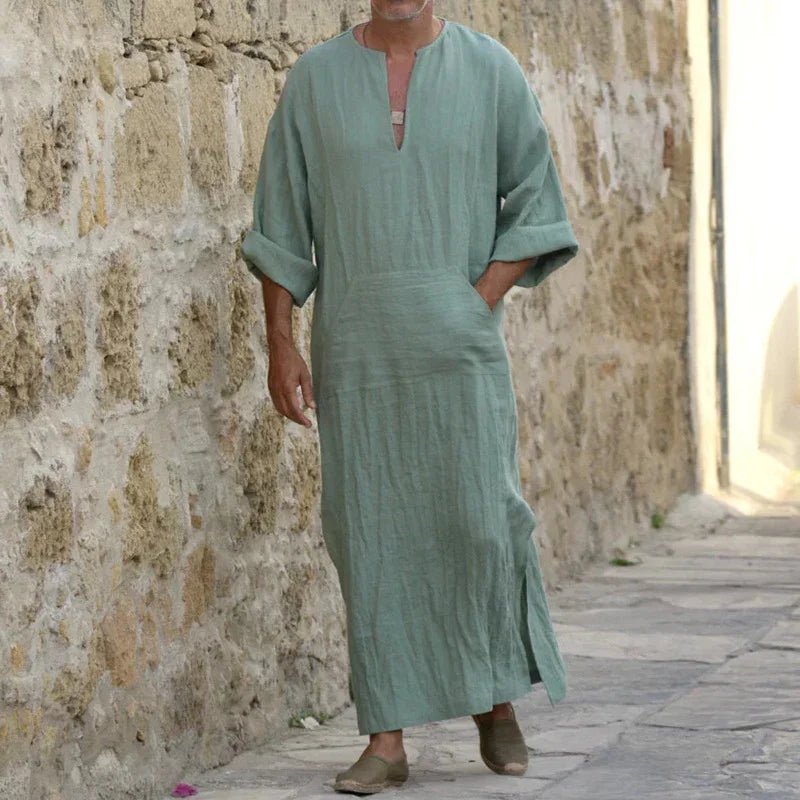 man wearing light green linen kaftan with rolled-up sleeves walking beside stone wall