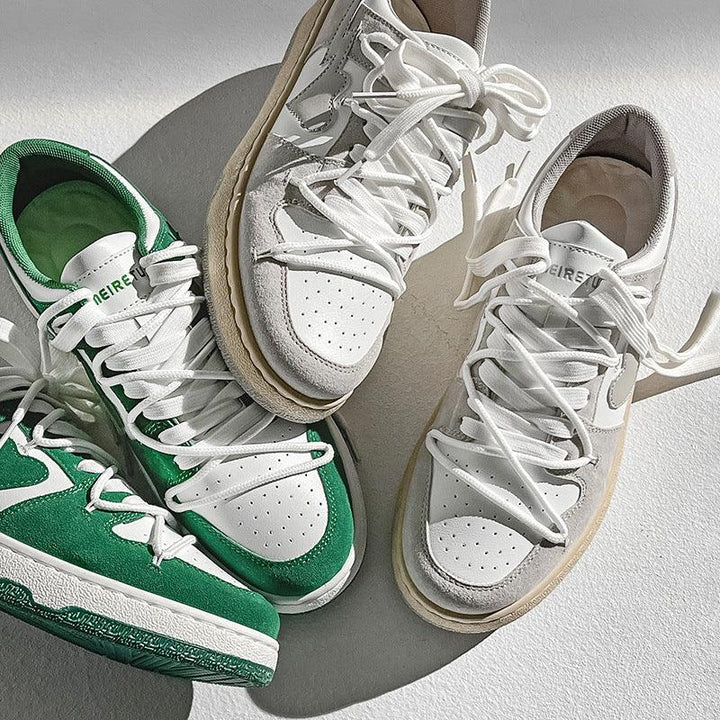 Pair of white sneakers with beige accents and white laces next to green and white sneakers on a white surface