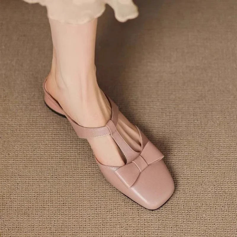 Woman wearing pink leather T-strap flat shoe with bow detail on textured brown floor