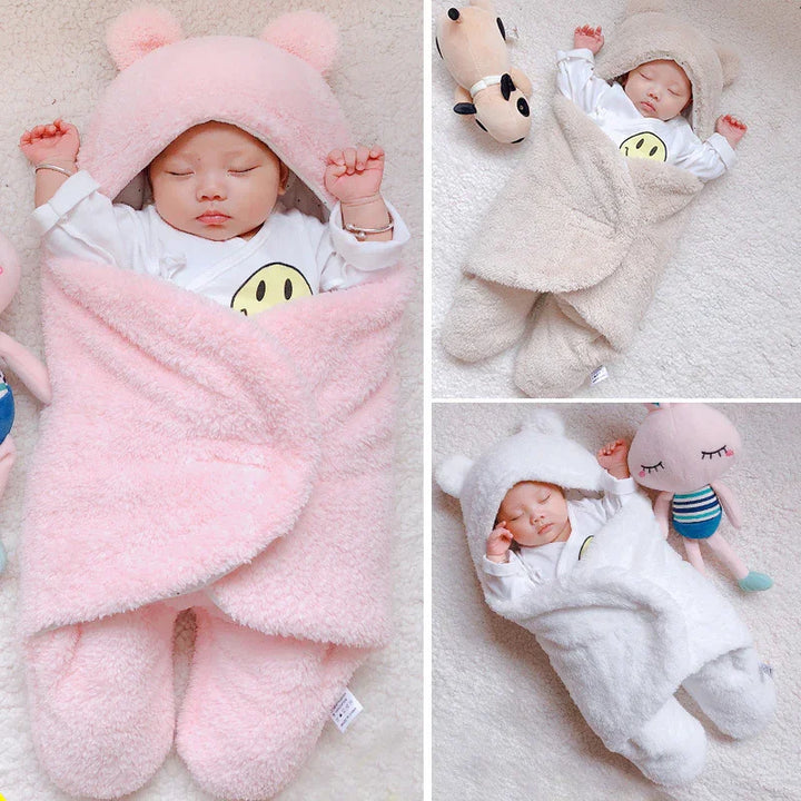 Sleeping baby wrapped in soft plush hooded blankets in pink, beige, and white on cozy carpet with toys