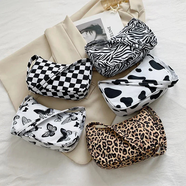Five stylish patterned shoulder bags with checkerboard, zebra, cow, butterfly, and leopard prints on beige fabric