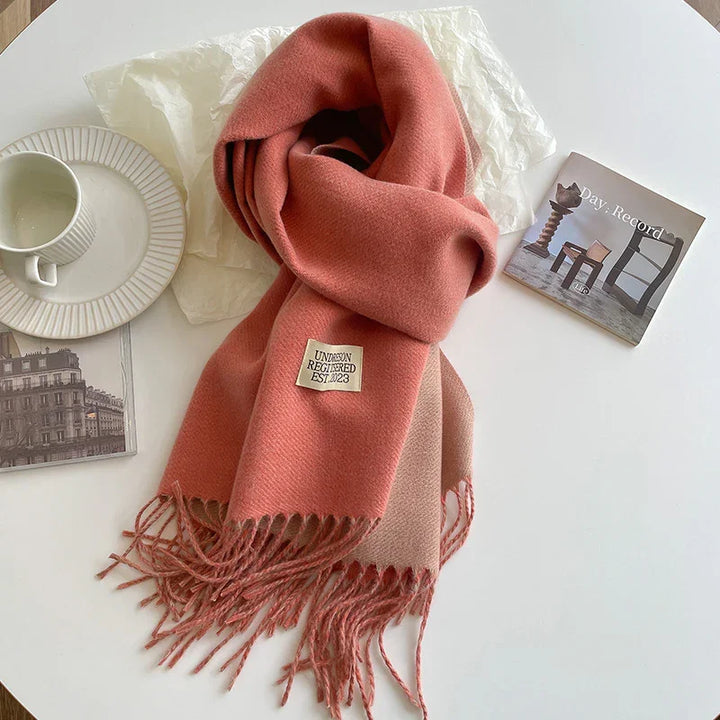 Soft coral pink wool scarf with fringes on white table next to ceramic cup and artistic photo cards