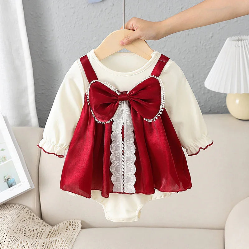 Cream long-sleeve baby dress with red satin bow and lace details hanging on wooden hanger