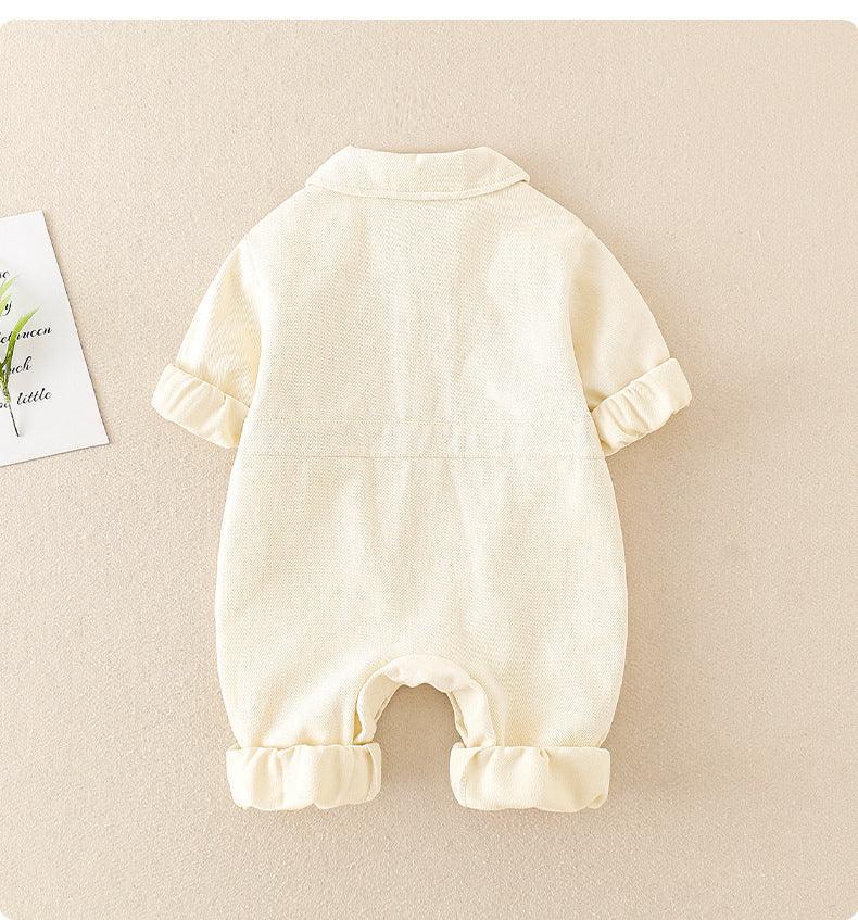 Cream-colored baby romper with folded sleeves and pant legs on beige background