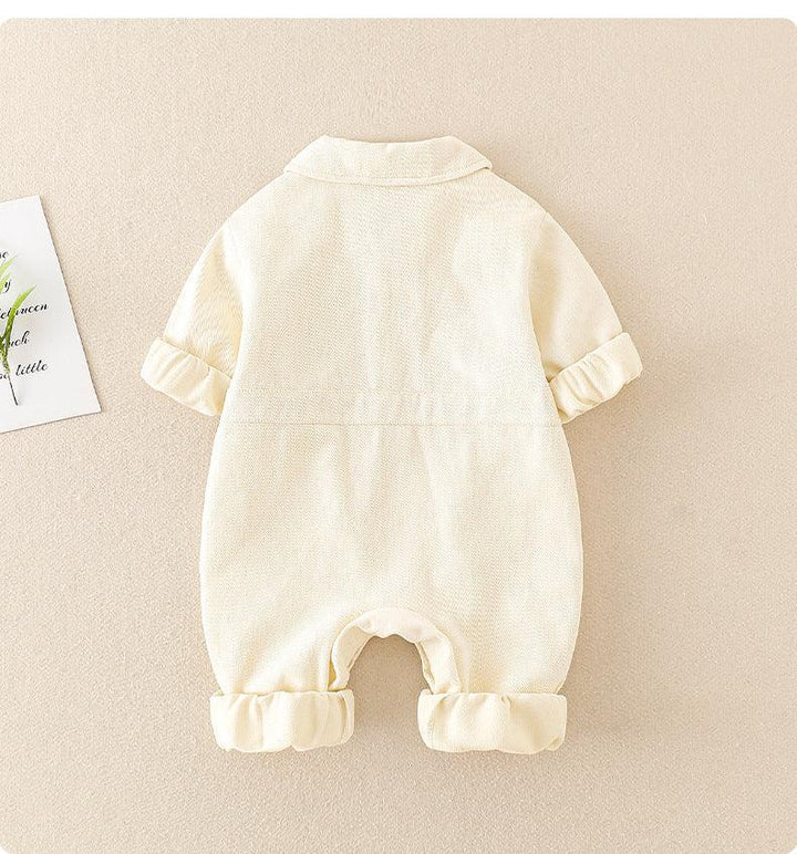 Cream-colored baby romper with folded sleeves and pant legs on beige background