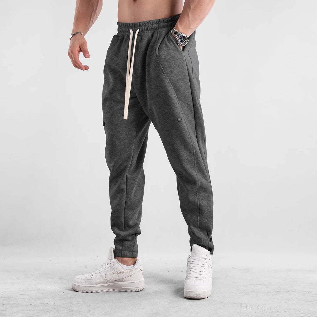 Male model wearing dark gray jogger pants with white drawstring and white sneakers against a plain background