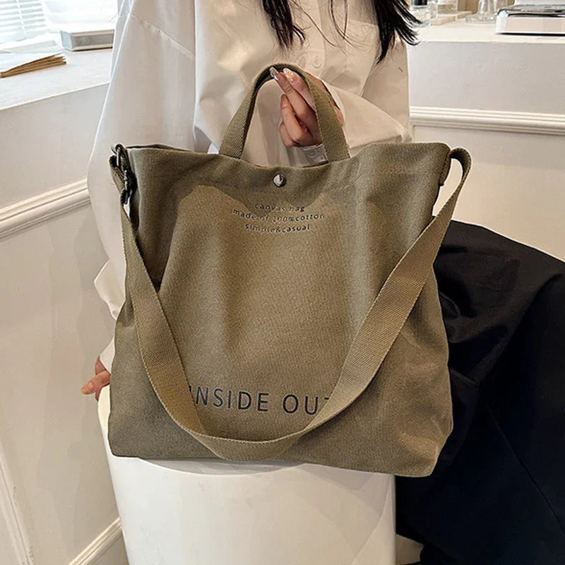 Woman holding large olive green canvas tote bag with shoulder strap and text inside out