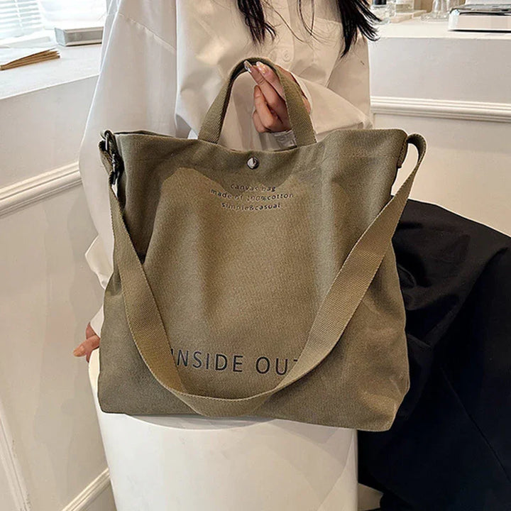 Woman holding large olive green canvas tote bag with shoulder strap and text inside out