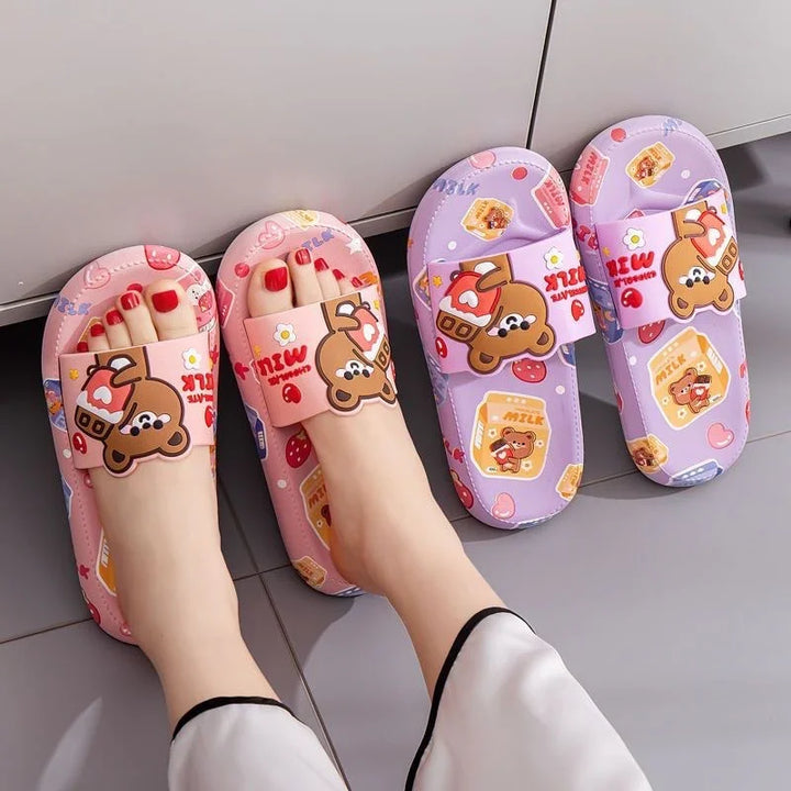 Person wearing pink cartoon bear slippers with milk carton and heart patterns, next to a purple pair on gray floor