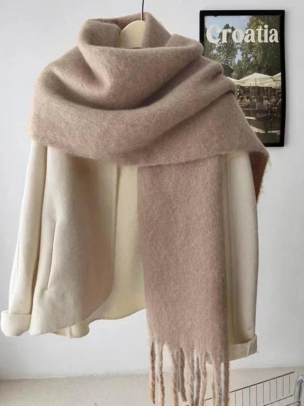 Beige wool scarf with fringes draped over cream coat on hanger with Croatia poster background